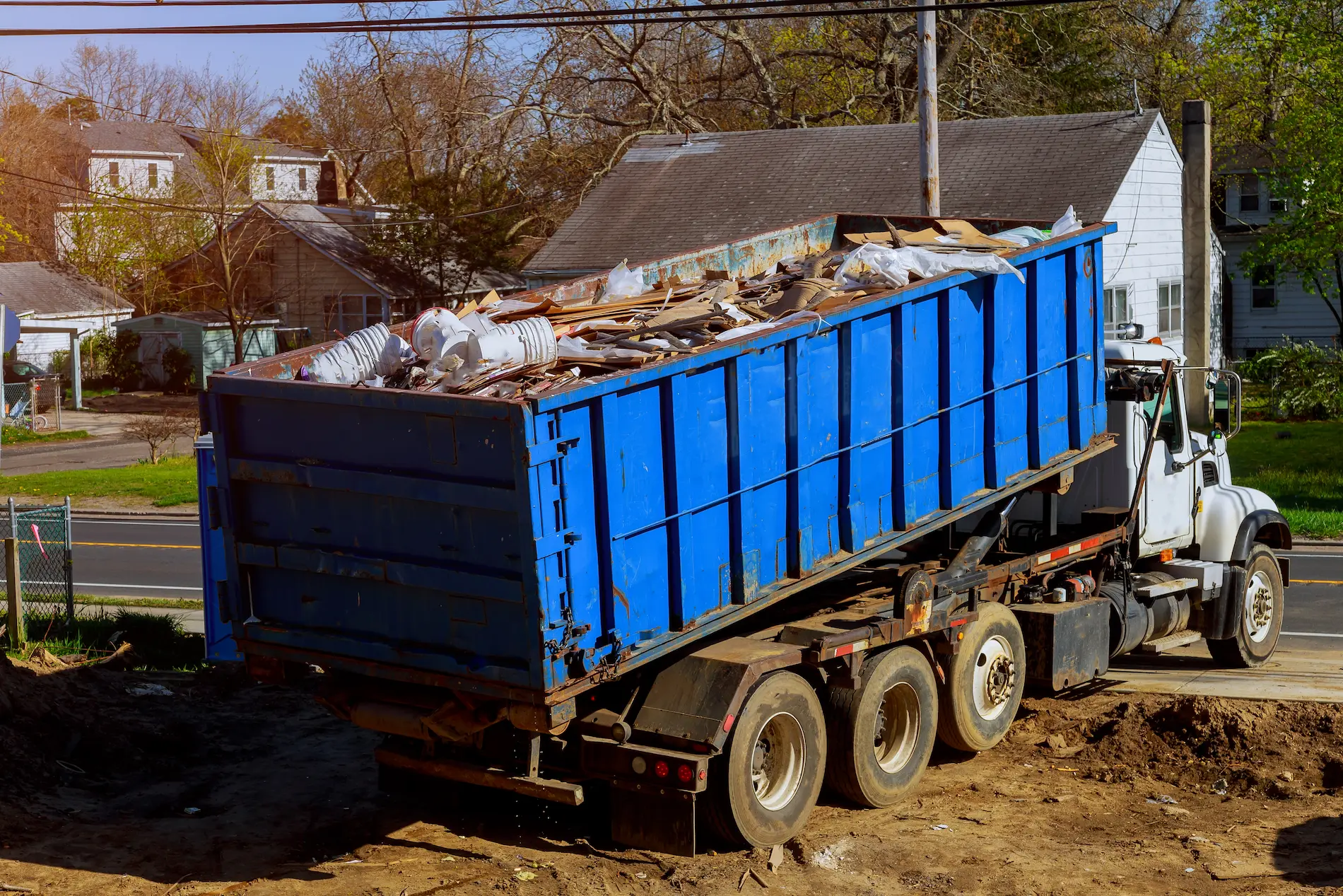 Blue Dumpster filled being rolled off by a truck