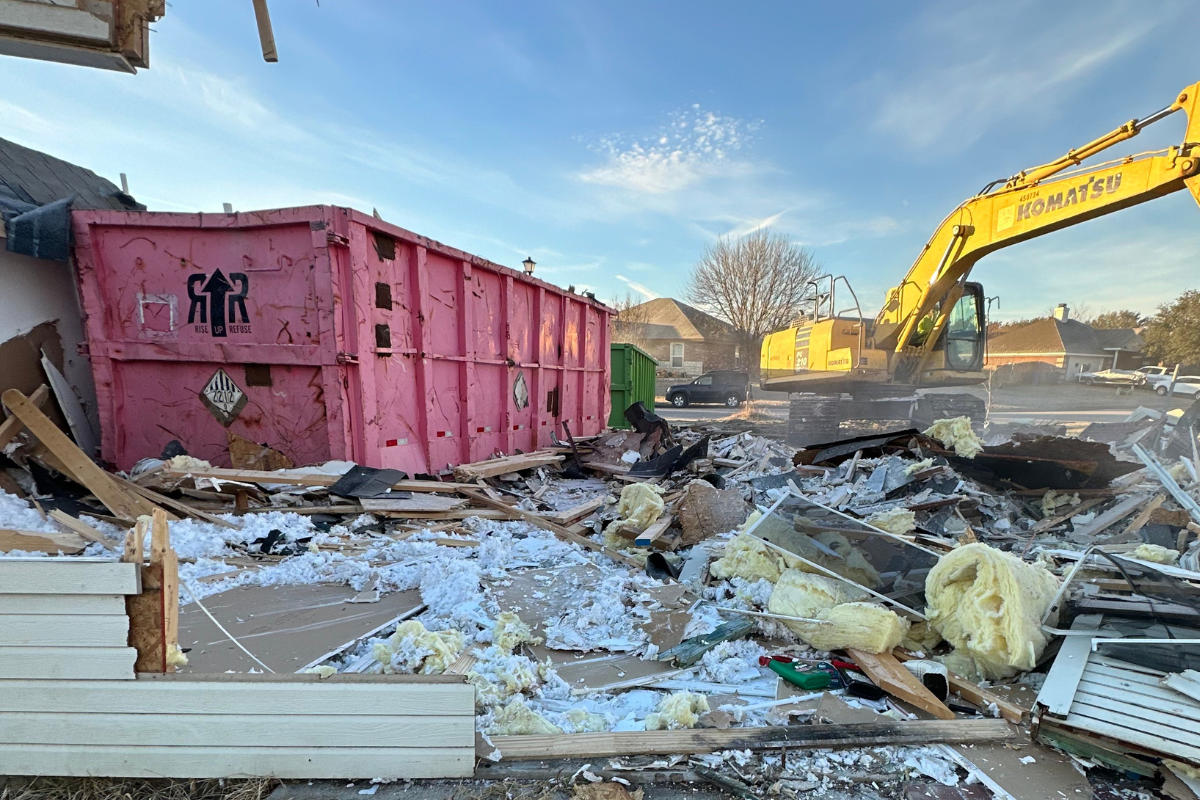 Red dumpster bin next to an excavator moving debris from home demolition