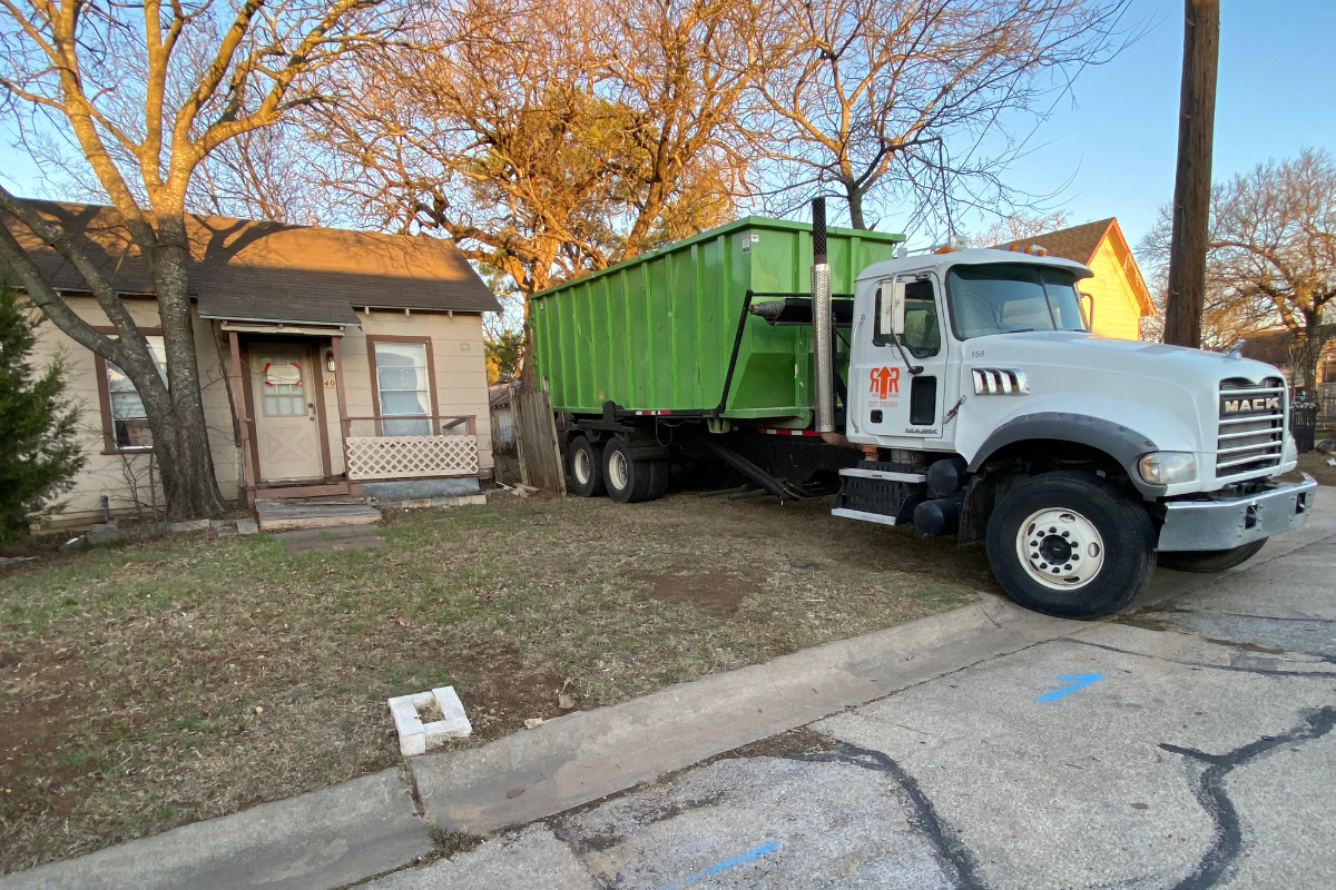 A truck with a green roll-off dumpster parked in residential lawn